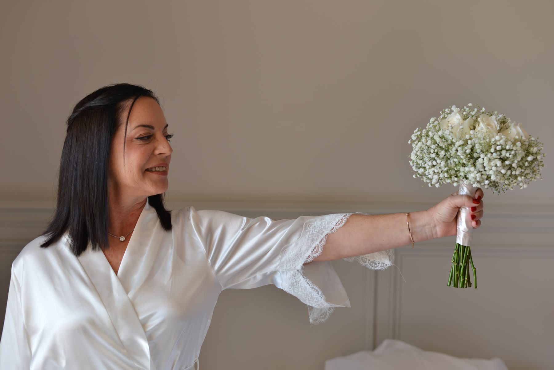 Novia sonriendo mientras sostiene su ramo de rosas blancas y paniculata